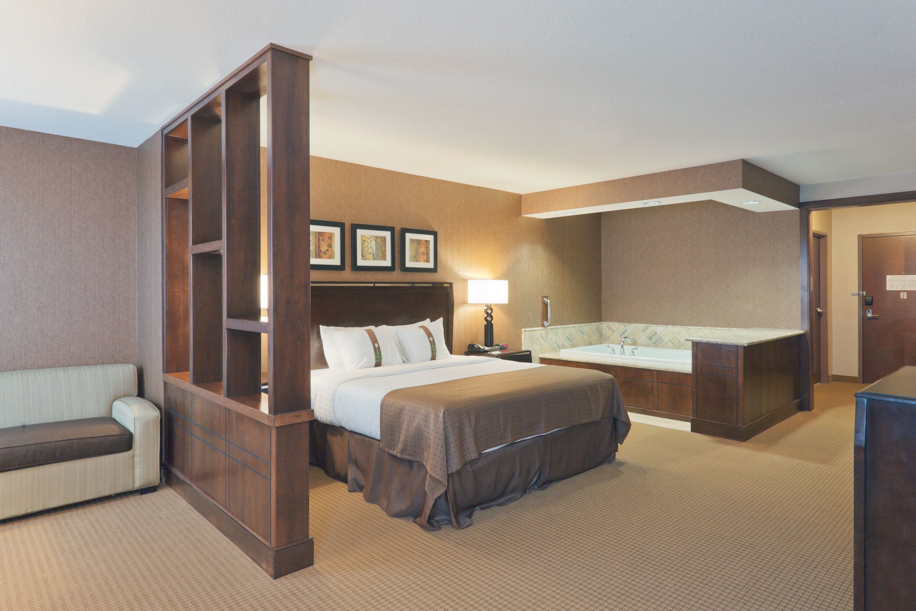 Une chambre d’hôtel comprenant un grand lit, un coin salon, un bureau, une salle de bain et une kitchenette.