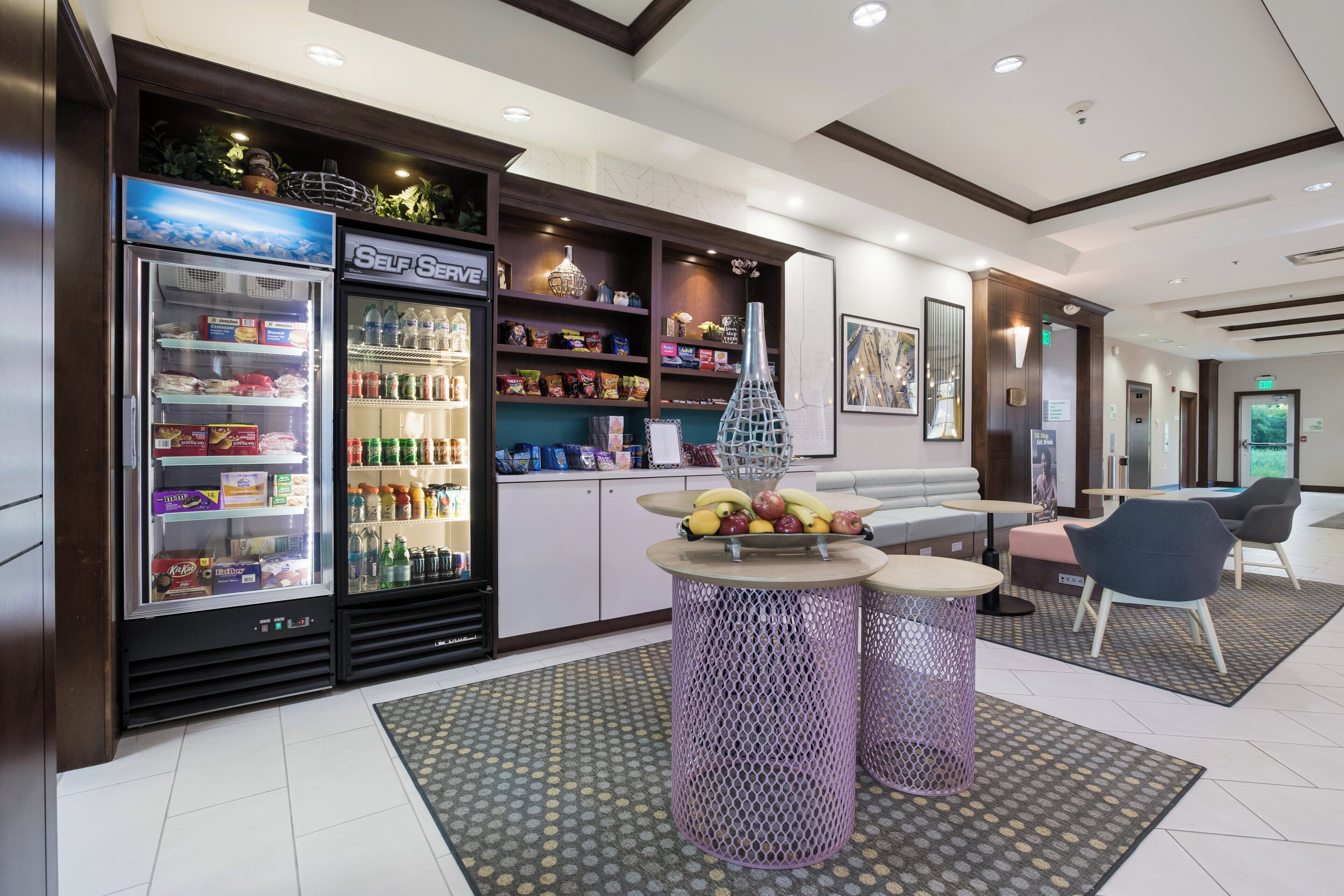 A hotel lobby with a self-service beverage station, seating area, and a reception desk.