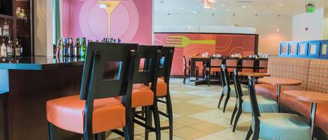 A bar area with stools and a counter, a seating area with tables and chairs, and a wall with a colorful design.