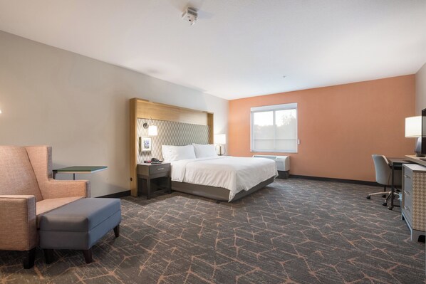 Quarto de hotel com cama, escrivaninha, cadeira, mesa de cabeceira e janela.