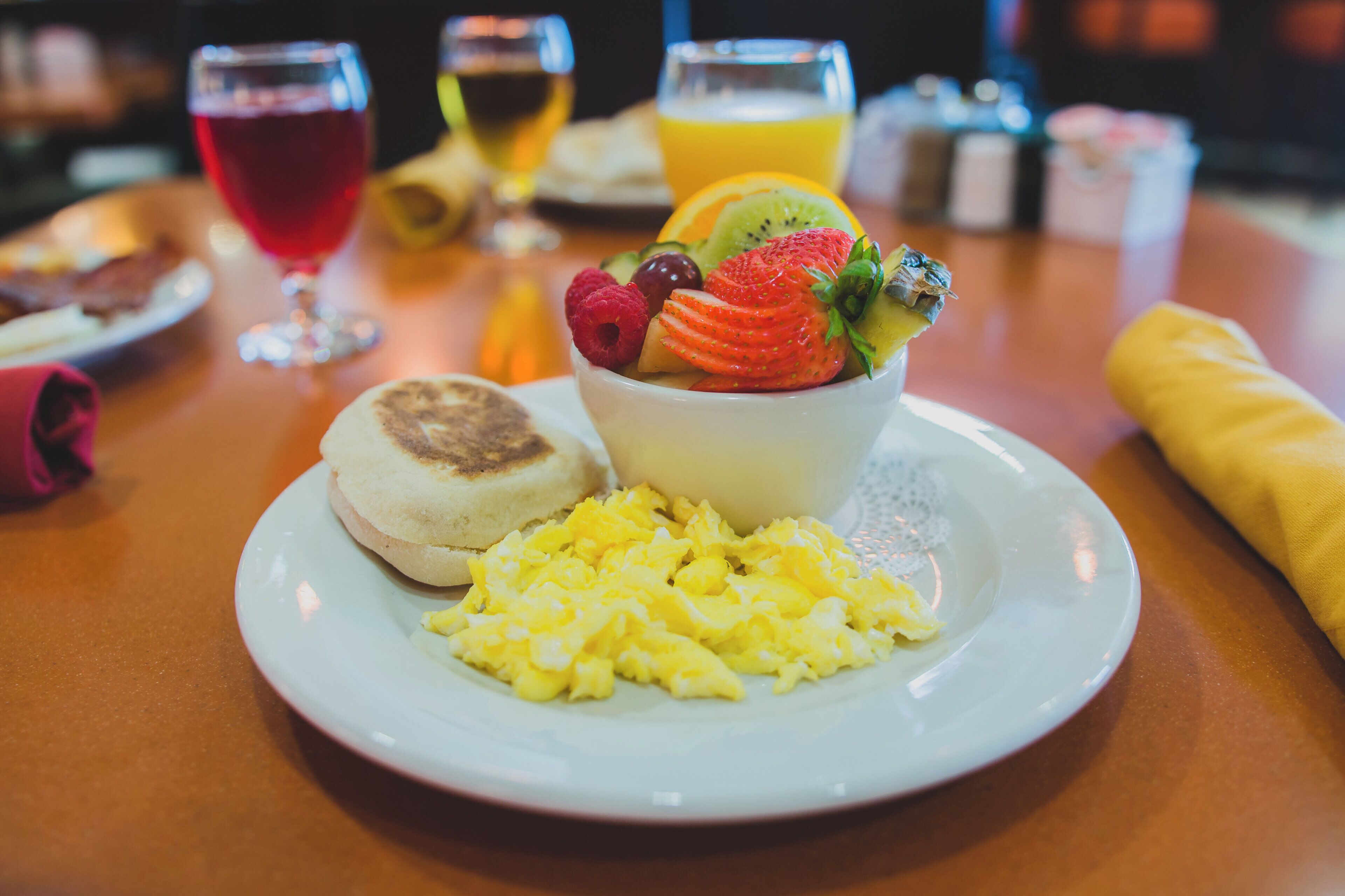 Une assiette de petit-déjeuner avec des œufs brouillés, un muffin et un saladier de fruits contenant des fraises, des framboises et des kiwis.