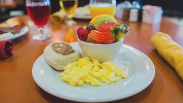 Une assiette de petit-déjeuner avec des œufs brouillés, un muffin et un saladier de fruits contenant des fraises, des framboises et des kiwis.
