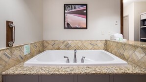 Un baño con una bañera blanca grande, un pasamanos, un cuadro de un coche rosa en la pared y un salpicadero de azulejos.