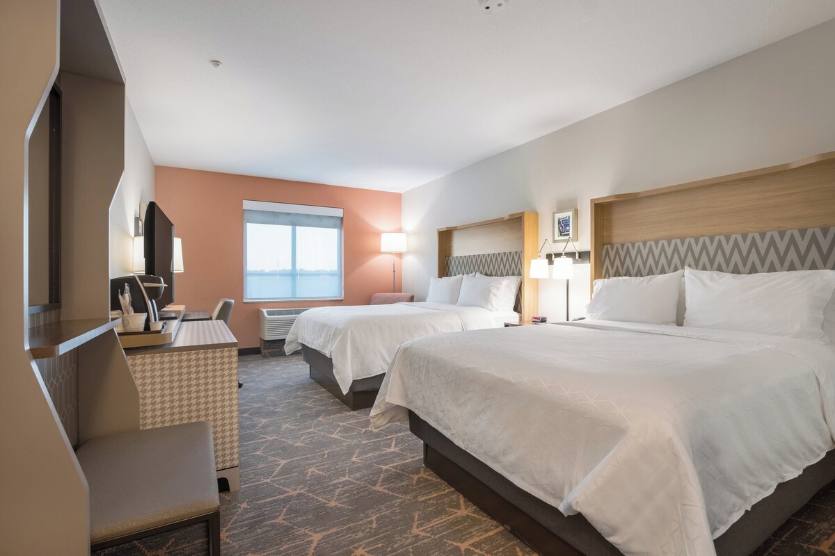 A hotel room with two beds, a desk, a chair, a TV, and a window with a view.