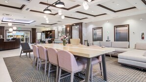 Un hall d’hôtel moderne avec une longue table à manger, plusieurs chaises, un canapé et un comptoir d’accueil.