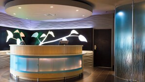 A reception area with a curved wooden desk, a modern light fixture, and a textured wall design. - SpringHill Suites by Marriott Quakertown (Quakertown)