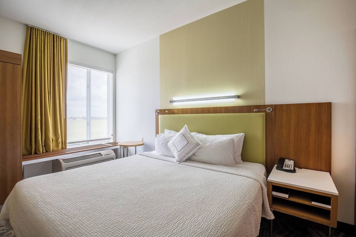 Een hotelkamer met een bed, nachtkastje en een raam met gordijnen.