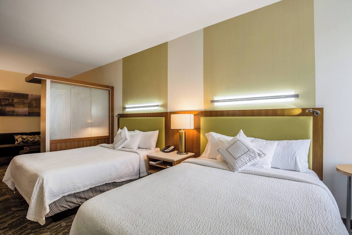 Een hotelkamer met twee bedden, een bureau, een lamp en een aan de muur bevestigde televisie.