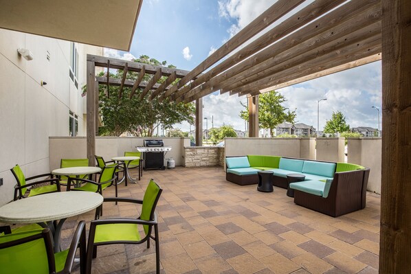 An outdoor patio with green and brown seating, a grill, and a pergola structure.