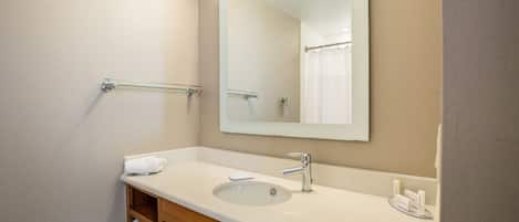 Un baño con lavamanos, espejo, toallero y repisa con toallas dobladas.