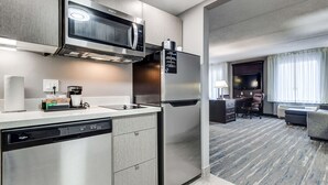 A modern kitchen with a built-in microwave, dishwasher, and refrigerator. There is a dining area with a table and chairs, and a living room with a couch and a flat-screen TV.