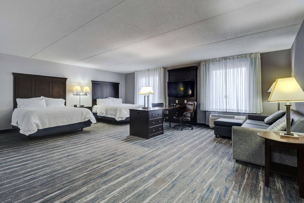 A hotel room with two beds, a desk, a chair, a TV, and a sofa.