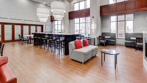 A spacious lobby with a bar area, seating arrangements, and large windows providing natural light.