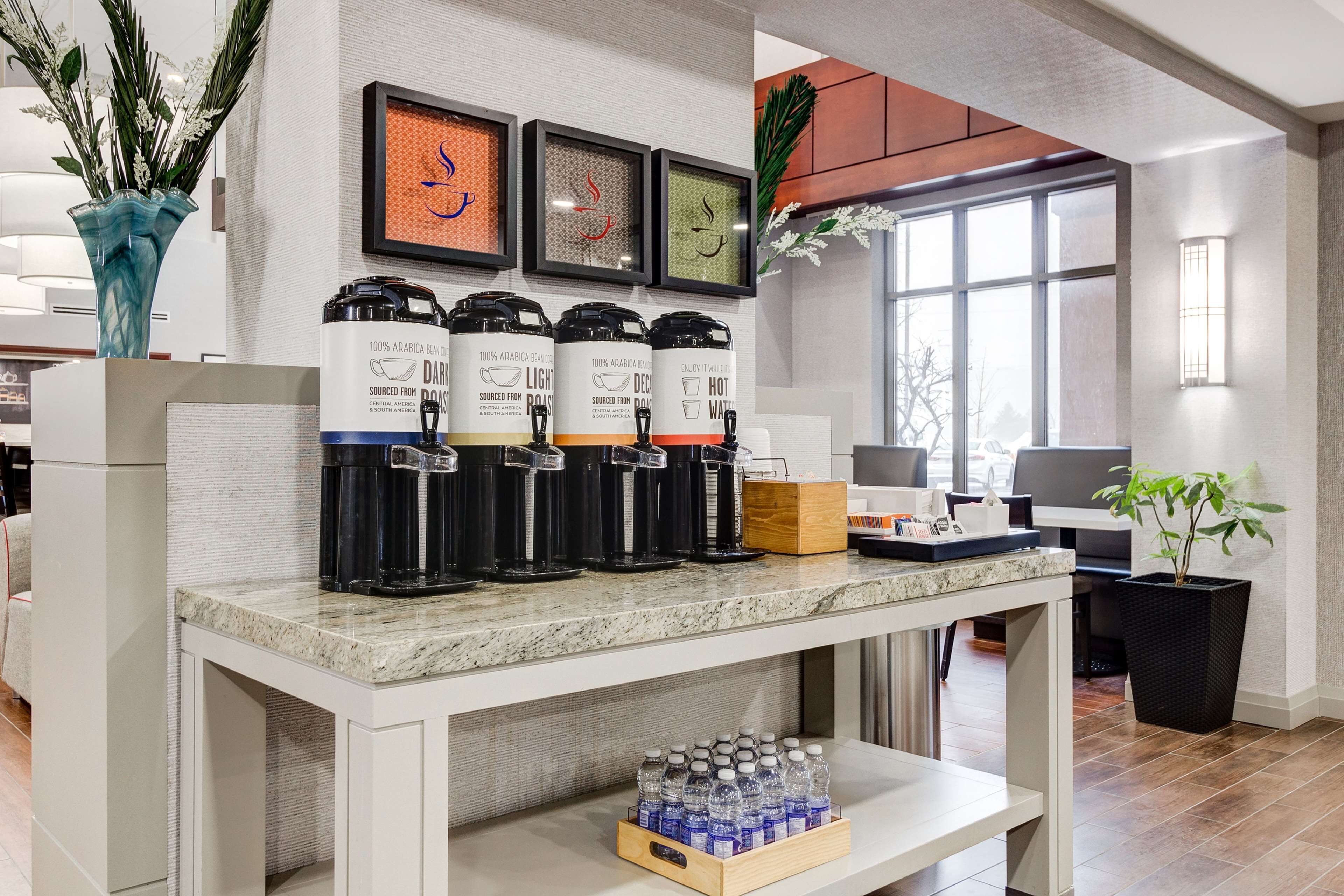 A coffee station with multiple coffee dispensers, a water dispenser, and a tray of bottled water.