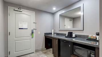 Un baño de hotel pequeño con una puerta blanca, un lavamanos, un espejo, un microondas y una cafetera.