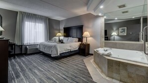 A modern hotel room with a large bed, bedside lamps, a built-in desk, a bathroom with a bathtub, and a large mirror.