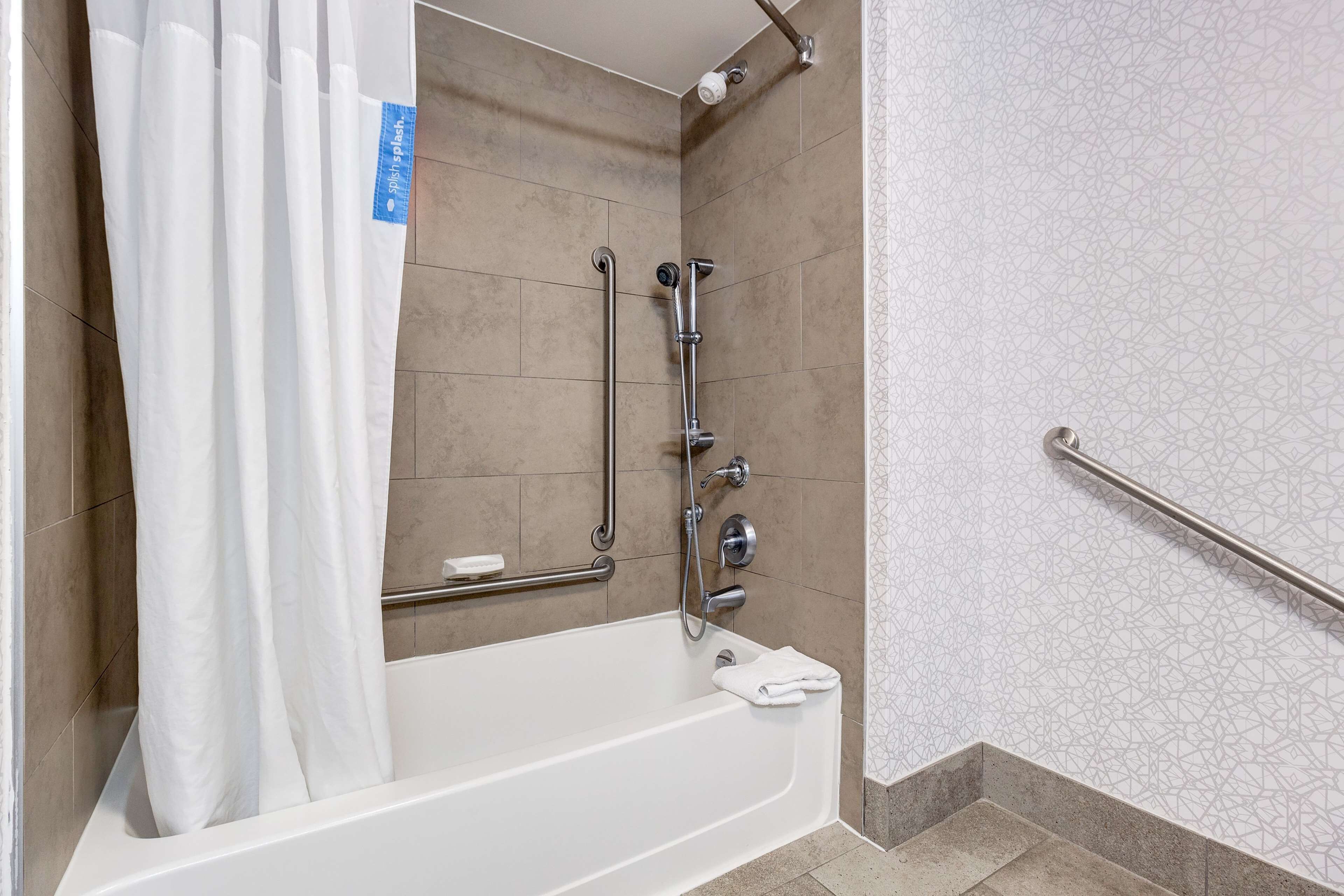 Un baño con bañera, barras de apoyo, cabezal de ducha y un perchero para toallas.