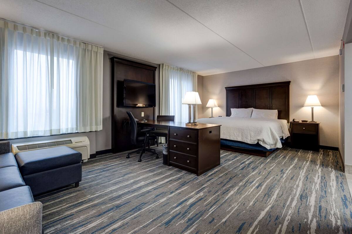 A hotel room with a bed, desk, chair, and two bedside lamps.
