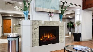 A modern lobby with a fireplace, a reception desk, and decorative plants.