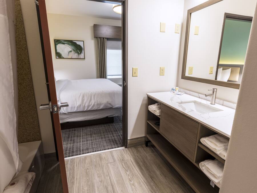 Una camera d'albergo con un letto, un bagno con lavandino e specchio, e una porta che dà su un'altra stanza.
