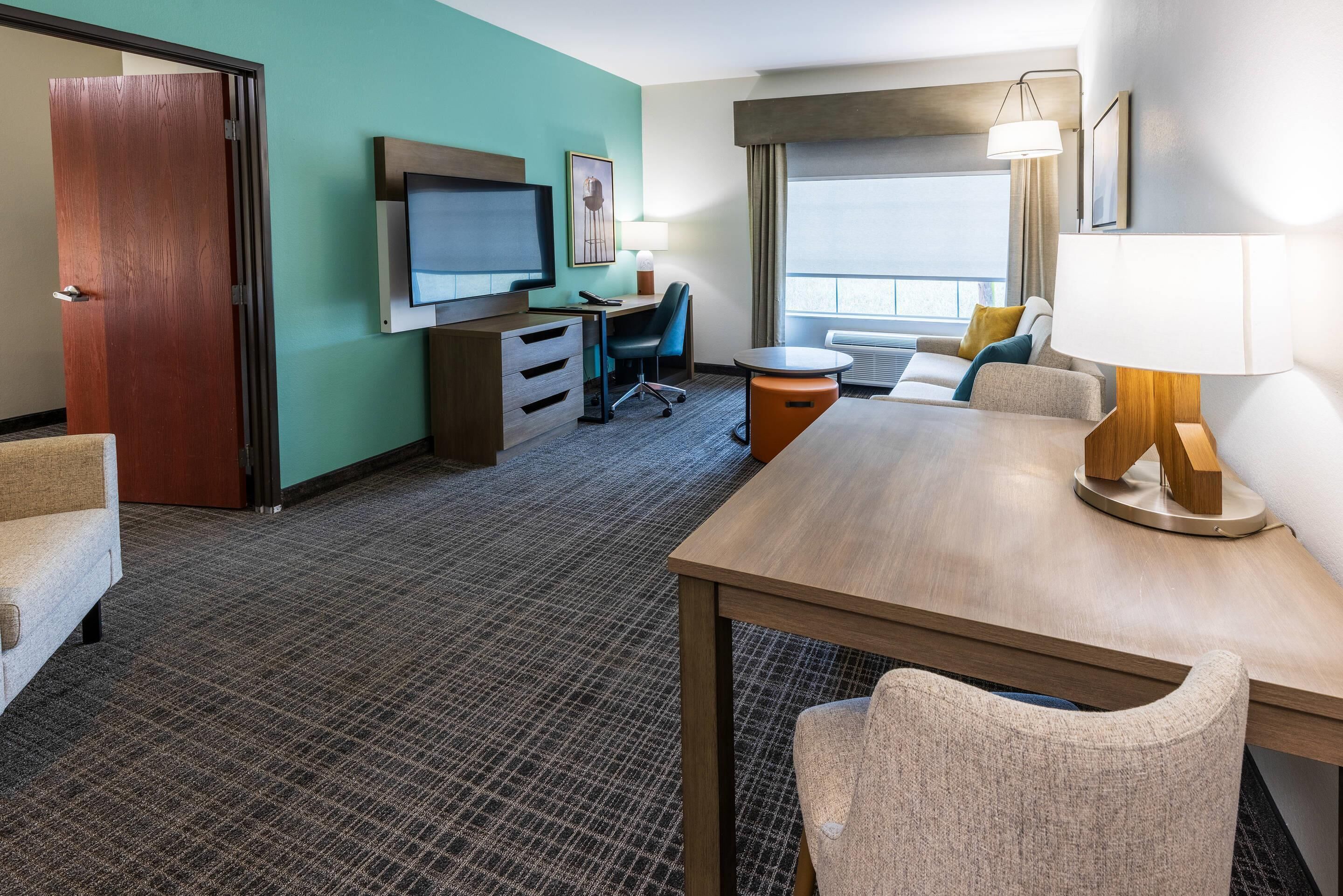 Une chambre d’hôtel équipée d’une télévision, d’un bureau, de chaises et d’une grande fenêtre.