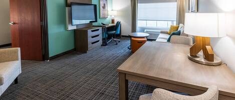 Une chambre d’hôtel équipée d’une télévision, d’un bureau, de chaises et d’une grande fenêtre.