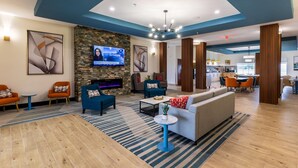 A modern hotel lobby with a stone fireplace, comfortable seating, a television, and a dining area.