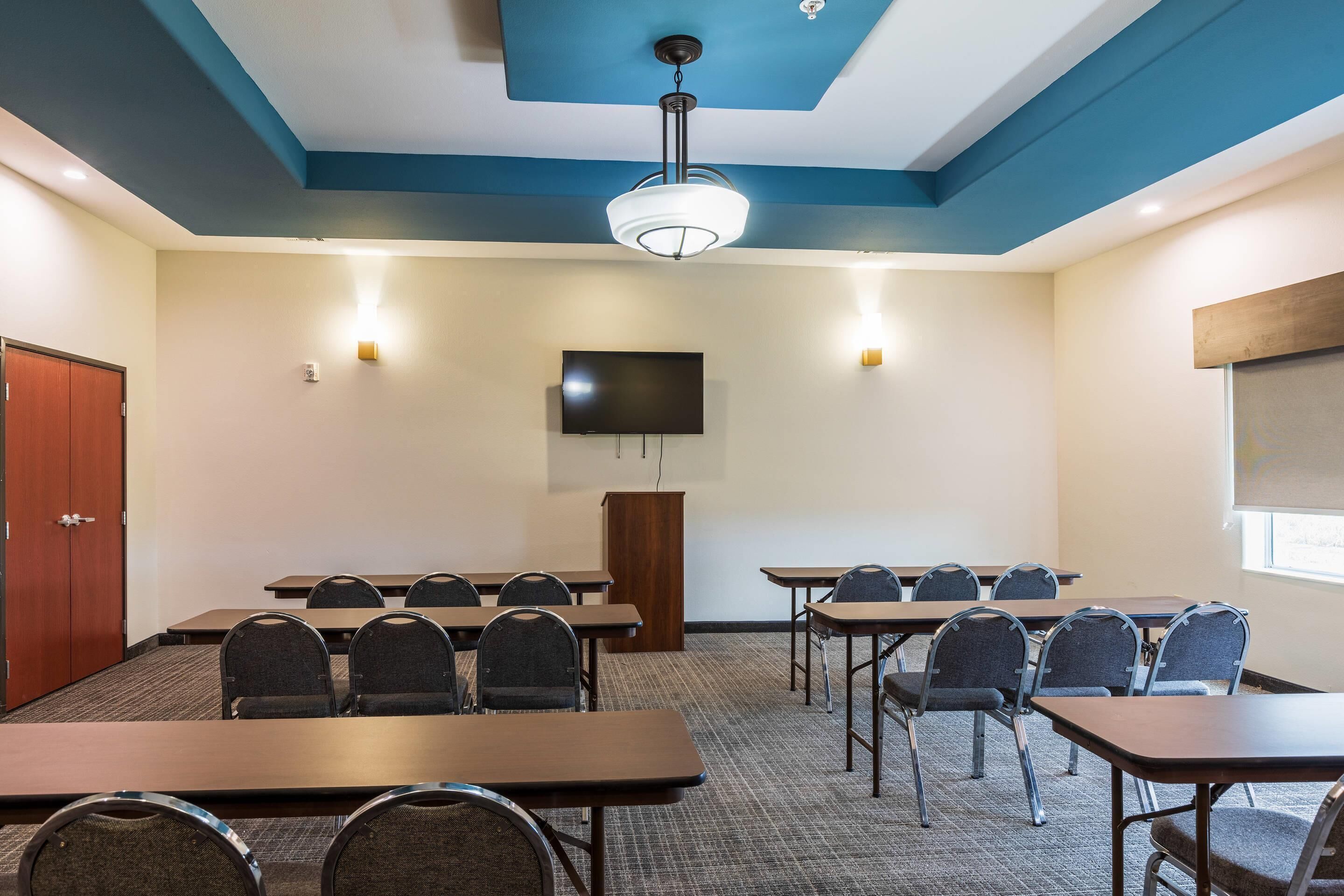 A conference room with tables, chairs, a podium, a TV, and a ceiling light.