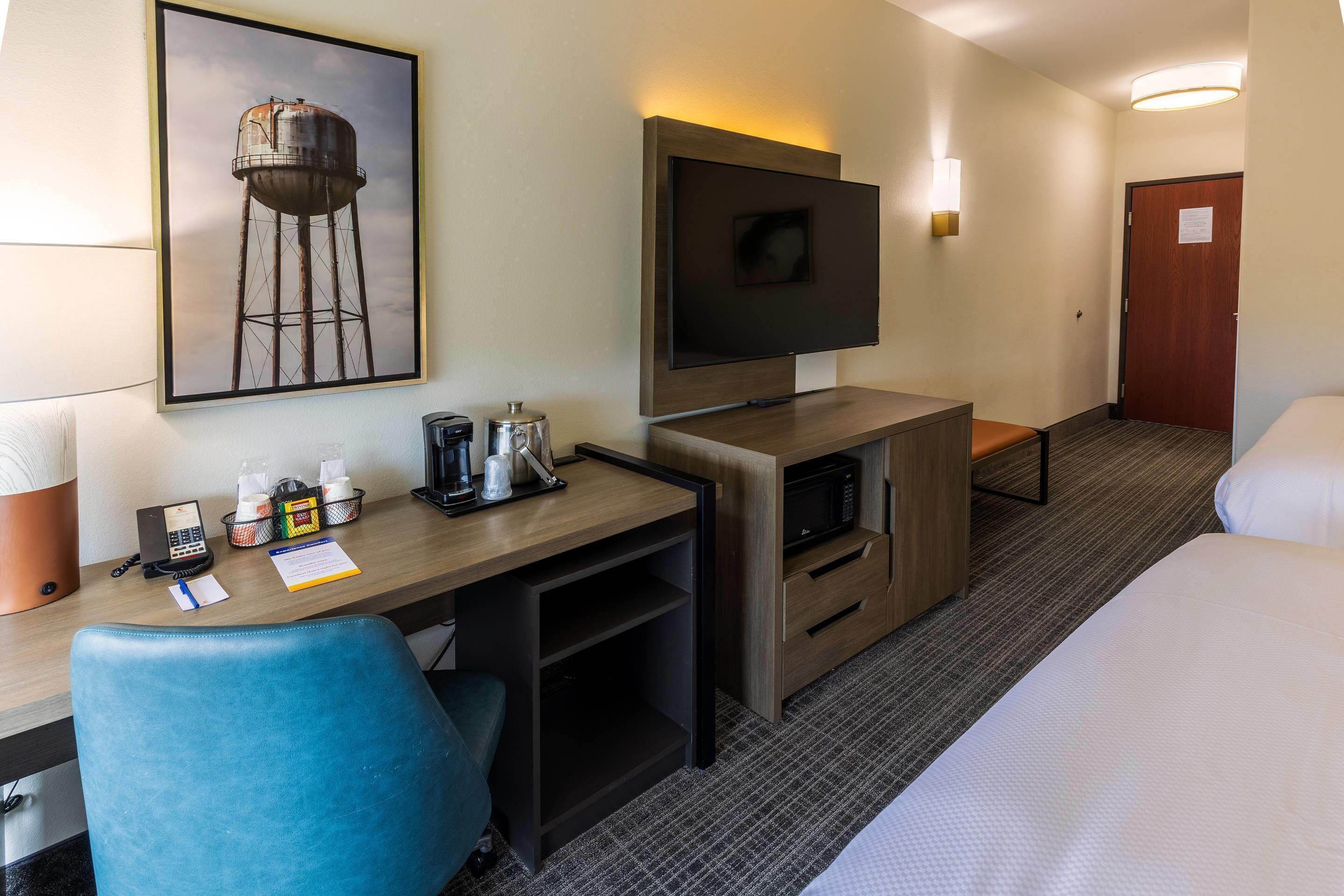 A hotel room with a desk, chair, TV, bed, and a framed picture on the wall.