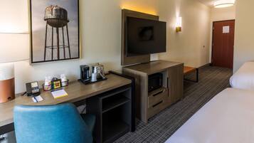 A hotel room with a desk, chair, TV, bed, and a framed picture on the wall.