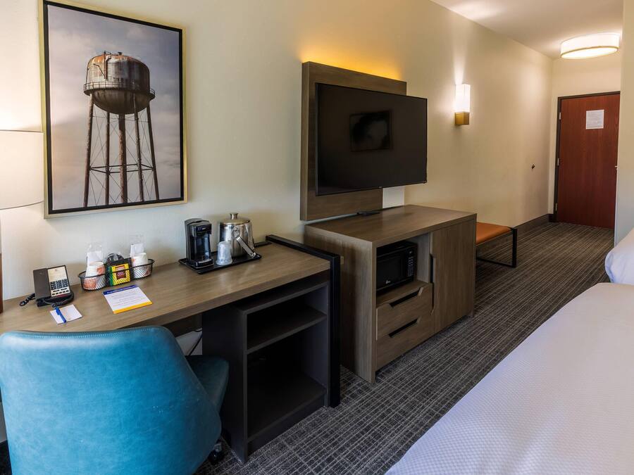 A hotel room with a desk, chair, TV, bed, and a framed picture on the wall.