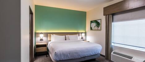 Ein Hotelzimmer mit Bett, Nachttischlampen, einer Wandklimaanlage und einem fenster mit Vorhängen.