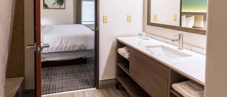 Une chambre d’hôtel comprenant un lit, une salle de bain avec un lavabo et un miroir, et une porte donnant sur une autre pièce.