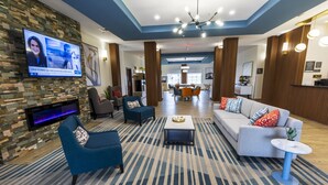 A modern hotel lobby with a stone wall, a flat-screen TV, seating areas, and a dining space.