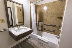 Een badkamer met een wastafel, spiegel, douche en handgrepen.