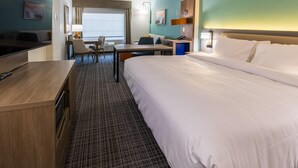 A hotel room with a large bed, a desk with a chair, a television, and a view of the outside.