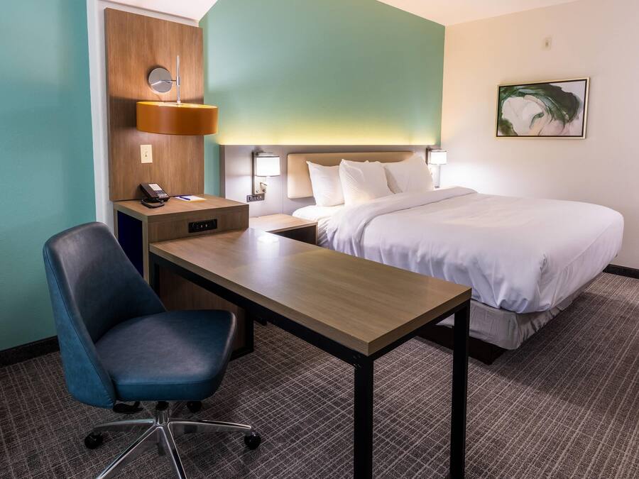 Habitación de hotel con cama, escritorio, silla, mesitas de noche y una lámpara fijada a la pared.