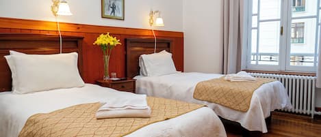 A hotel room with two beds, wooden headboards, white bedding, and a large window with a view of buildings.