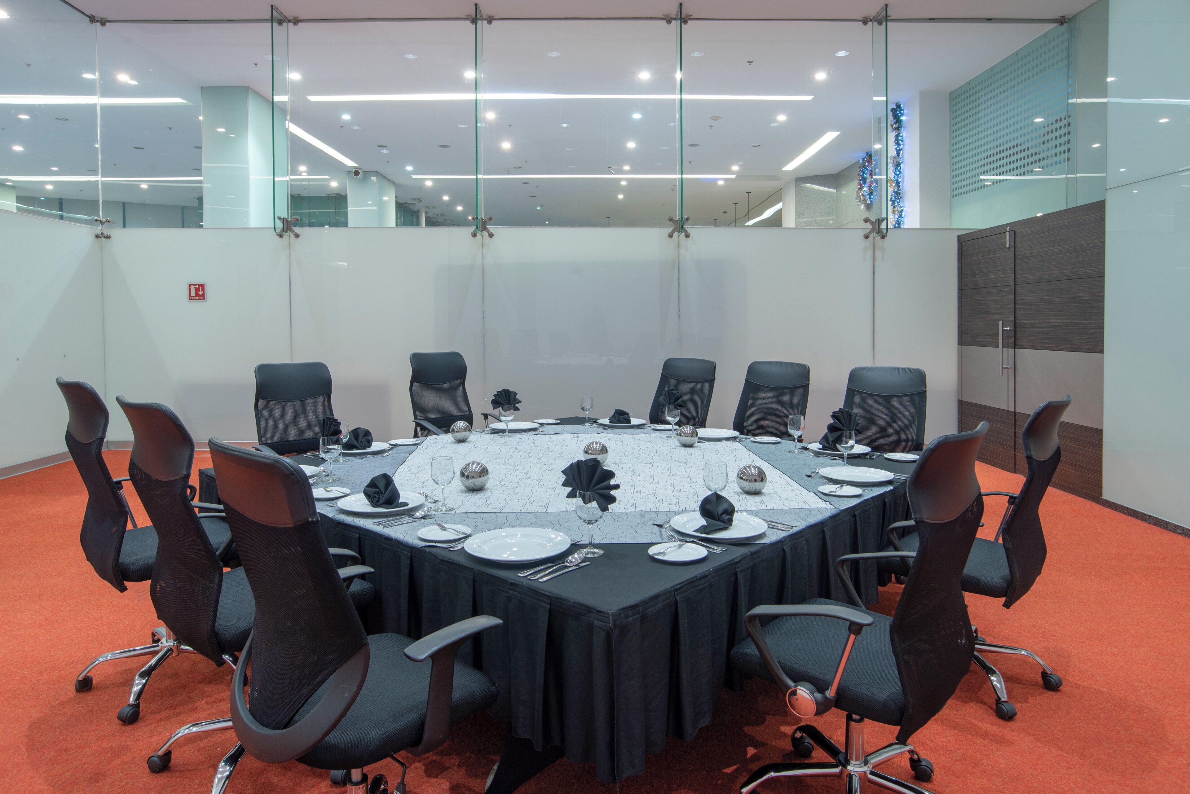 A conference room with a round table, black chairs, and a glass partition.