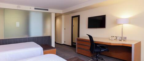 A hotel room with two beds, a desk, a chair, a flat-screen TV, and a lamp.