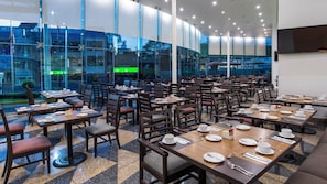 A hotel dining area with multiple tables and chairs, large windows, and a view of the cityscape. - Holiday Inn Mexico City - Plaza Universidad by IHG (Mexico City)