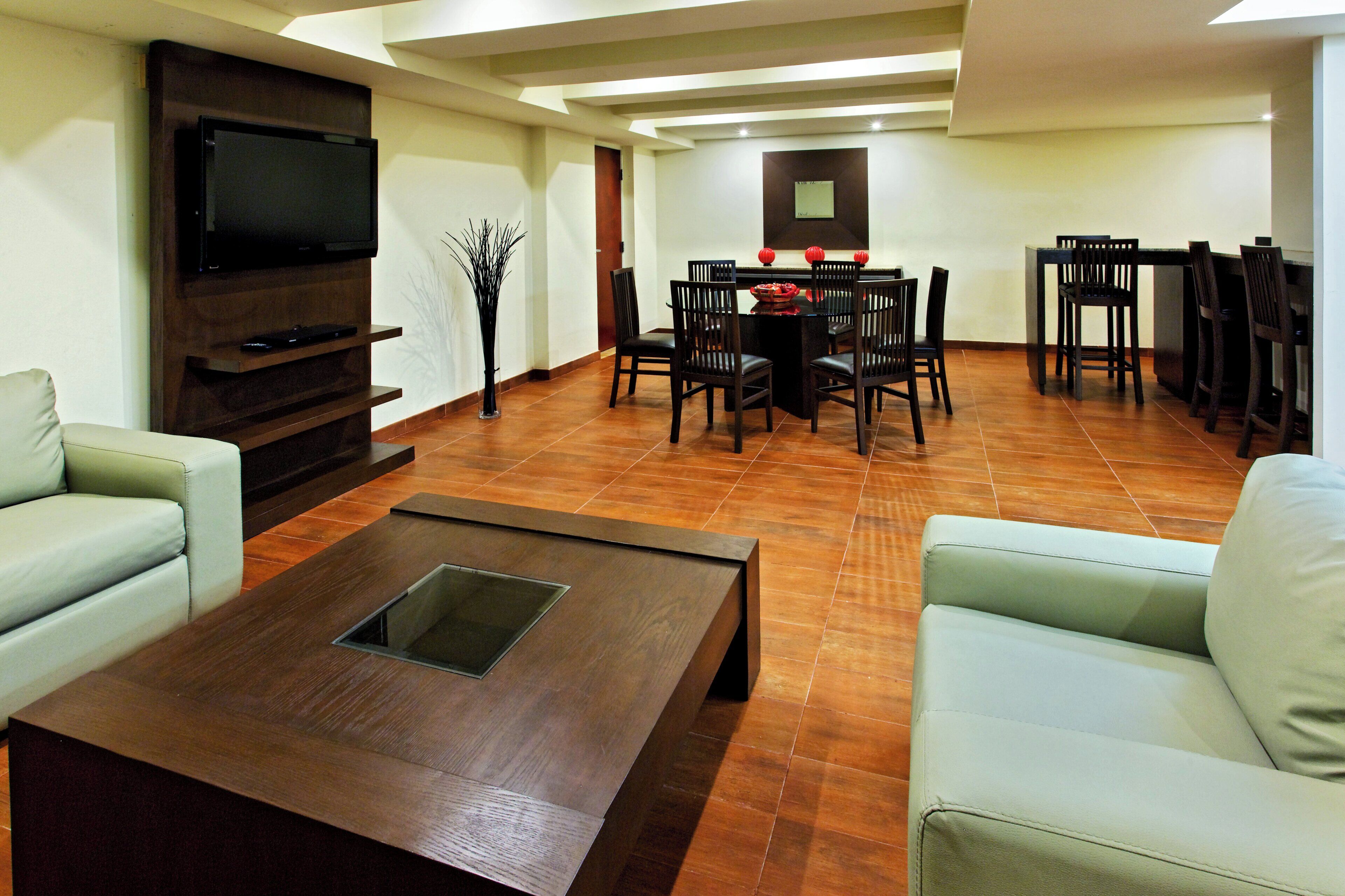 A living room with a flat-screen TV, a coffee table, and a dining area with chairs and a table.