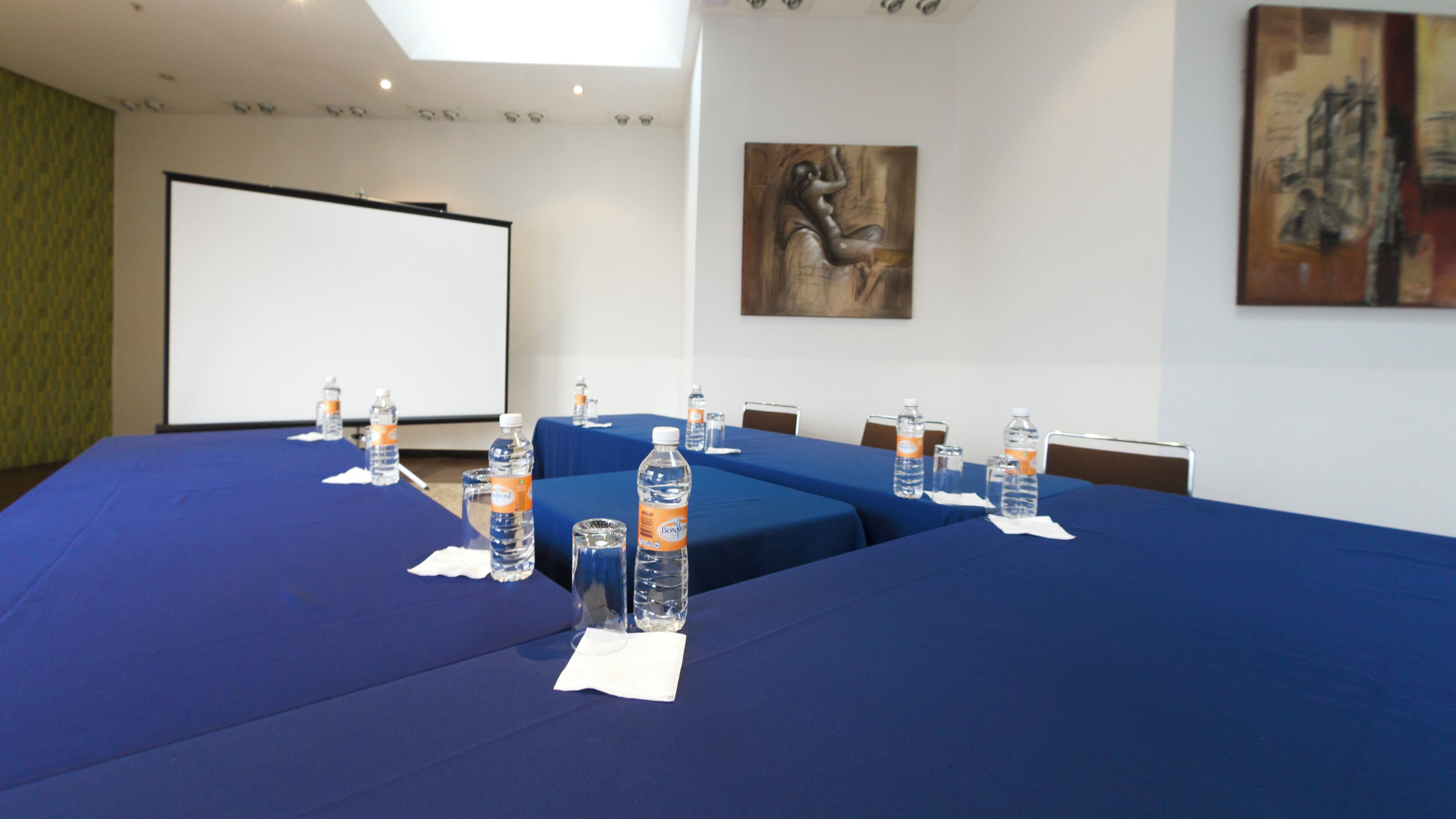 Sala de conferência com uma mesa comprida, garrafas de água e um projetor.