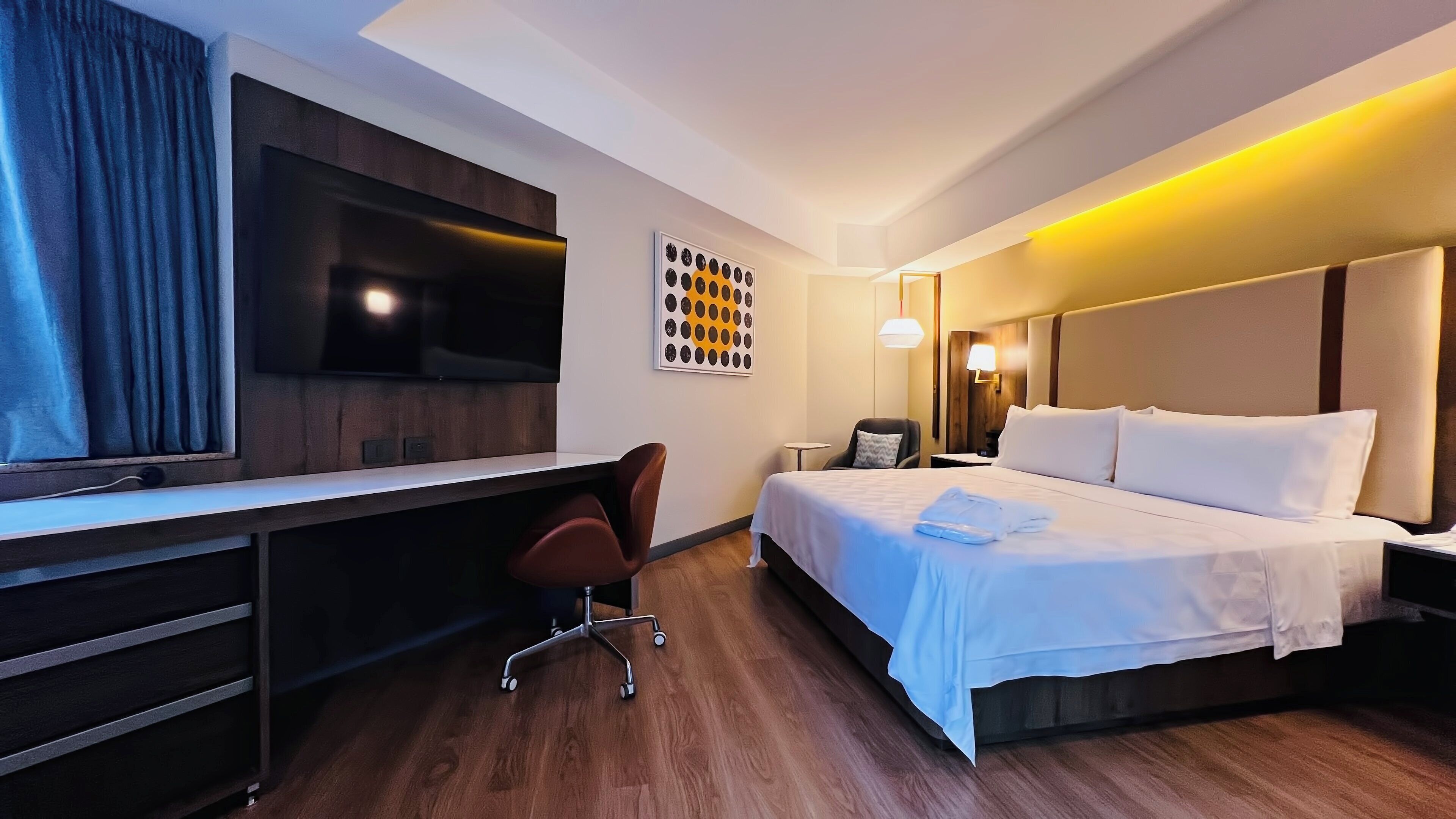Een hotelkamer met een bed, bureau, stoel, televisie en kunst aan de muur.