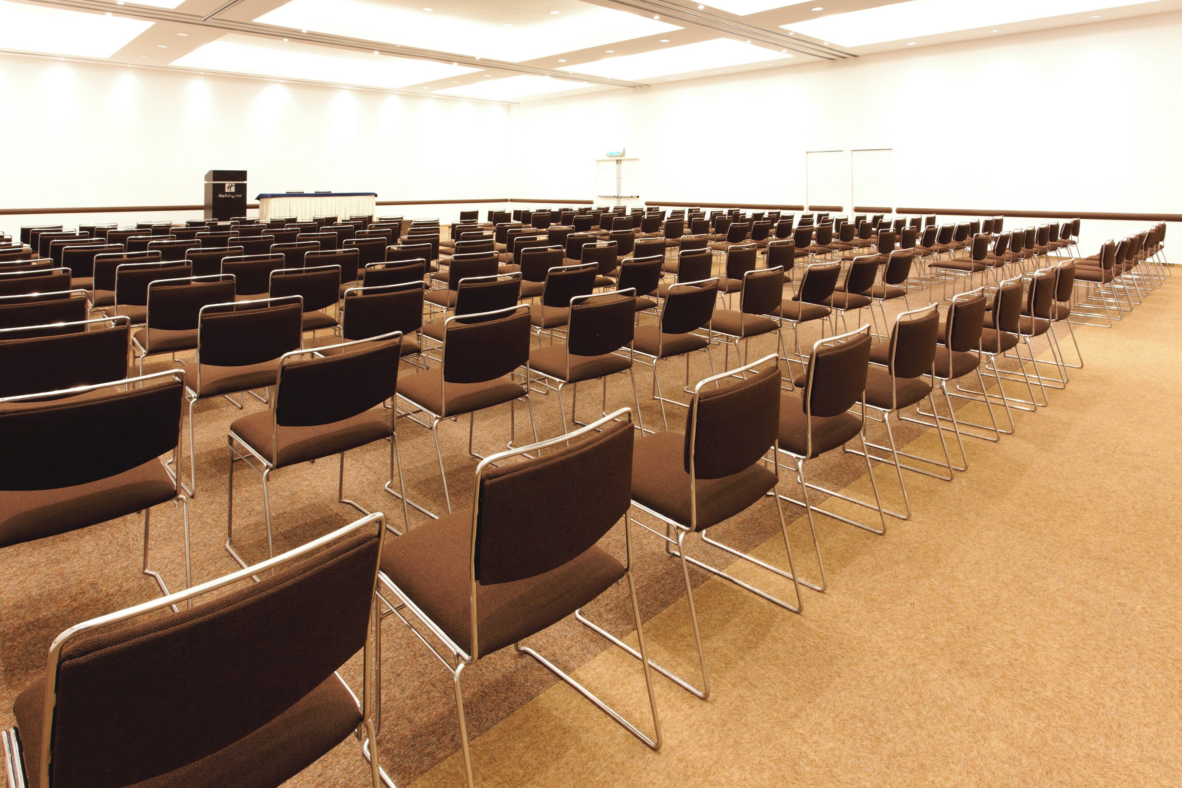 Une salle de conférence avec des rangées de chaises et un pupitre à l’avant.