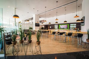 Eine moderne Bar mit hohen Hockern, Topfpflanzen und einem großen Bildschirm.