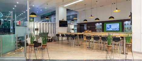 Zona de bar moderna con diversas opciones de asientos, una pantalla de televisión y una variedad de botellas en estanterías.