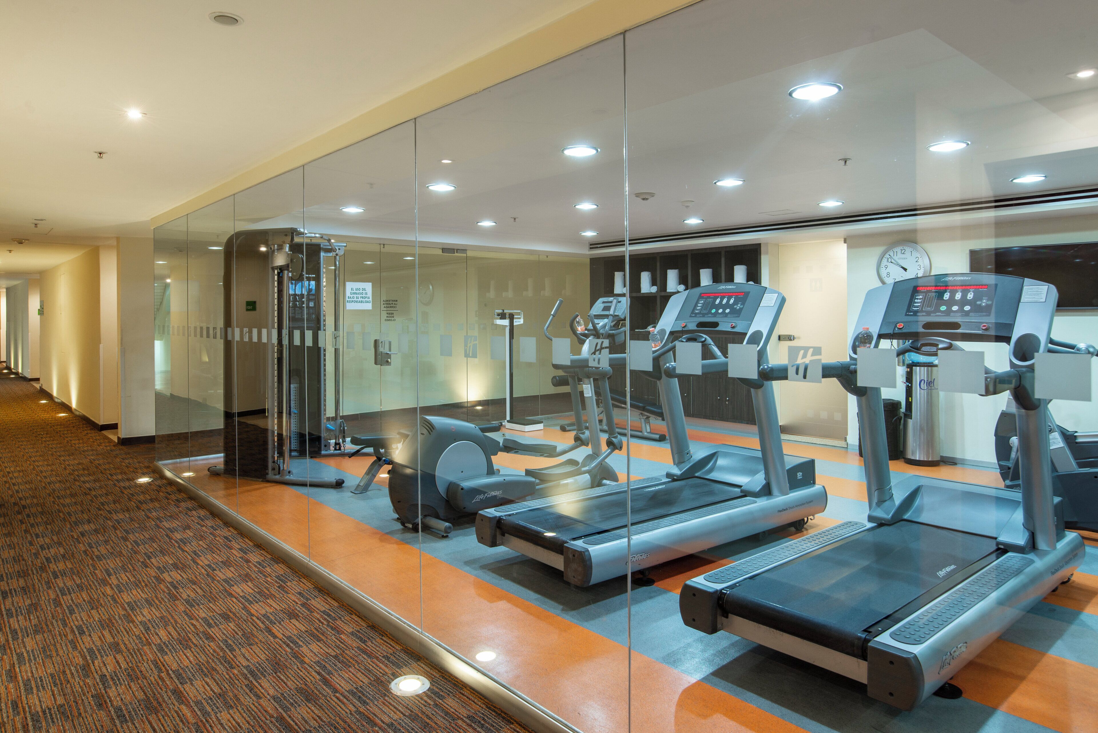 A gym with treadmills, exercise bikes, and a mirrored wall.