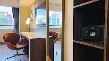 A modern hotel room with a desk, two chairs, a lamp, and a minibar.