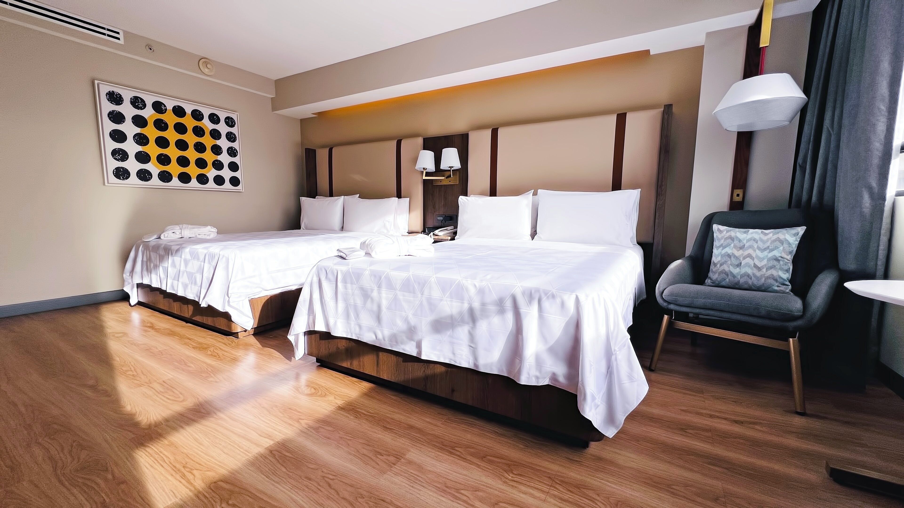 A hotel room with two beds, a chair, a table, and a wall art piece.